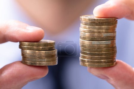 Photo for Man Holding Two Coin Stacks To Compare - Royalty Free Image
