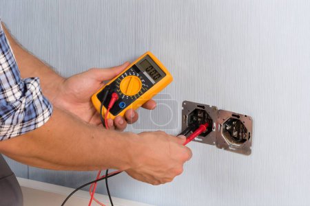 Photo for Male Electrician Checking Voltage Of Socket With Multimeter In House - Royalty Free Image