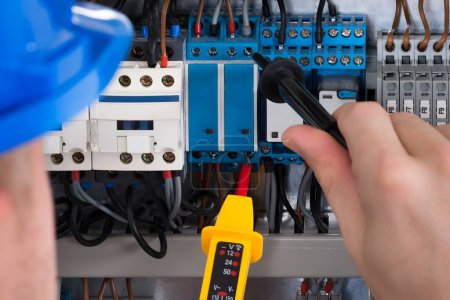 Photo for Male Electrician Examining Fusebox With Voltage Tester - Royalty Free Image