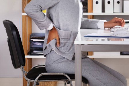Foto de Joven empresaria que sufre de dolor de espalda mientras trabaja en la oficina - Imagen libre de derechos