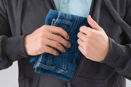 Mann versteckt Jeans in Jacke im Geschäft