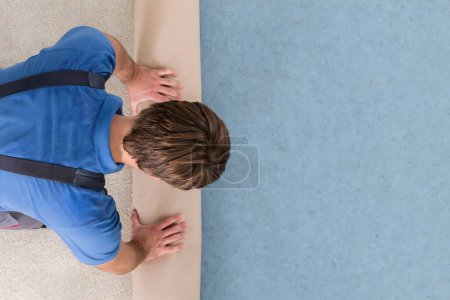 Foto de Vista de ángulo alto del trabajador en uniforme desenrollando la alfombra en el piso - Imagen libre de derechos