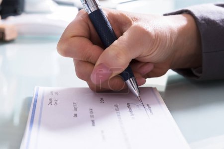 Téléchargez les photos : Gros plan de la main d'un homme d'affaires signant un chèque avec stylo au bureau - en image libre de droit