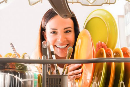 Photo for Young Happy Woman Arranging Plates In Dishwasher - Royalty Free Image