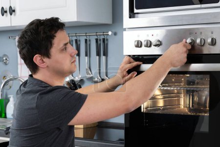 Foto de Hombre discapacitado usando horno de microondas para hornear en la cocina - Imagen libre de derechos