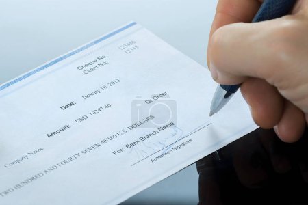 Foto de Primer plano de la mano del empresario que llena el cheque en blanco en el escritorio - Imagen libre de derechos