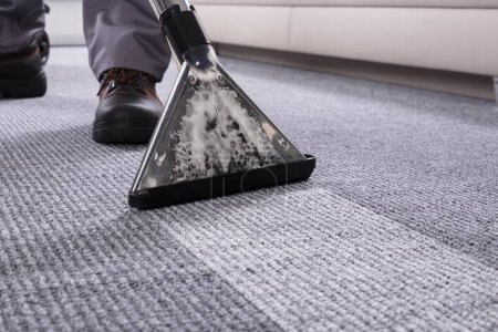 Foto de Sección baja de una persona limpiando la alfombra con aspiradora en la sala de estar - Imagen libre de derechos