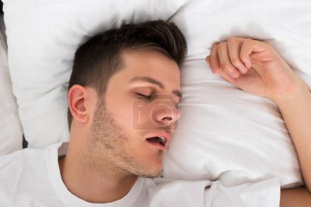 Téléchargez les photos : Vue D'un jeune homme fatigué ronflant pendant qu'il dormait profondément au lit - en image libre de droit