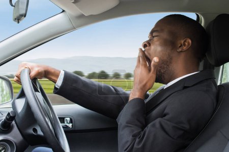 Foto de Vista lateral de un joven empresario africano bostezando mientras conduce un coche - Imagen libre de derechos