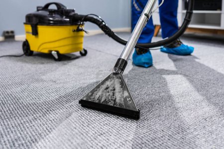 Téléchargez les photos : Photo de concierge nettoyage tapis avec aspirateur - en image libre de droit