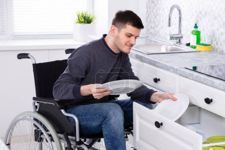 Téléchargez les photos : Jeune homme handicapé heureux assis sur des plaques d'arrangement en fauteuil roulant dans le tiroir - en image libre de droit