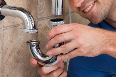 Téléchargez les photos : Jeune plombier mâle montage tuyau d'évier dans la salle de bain - en image libre de droit
