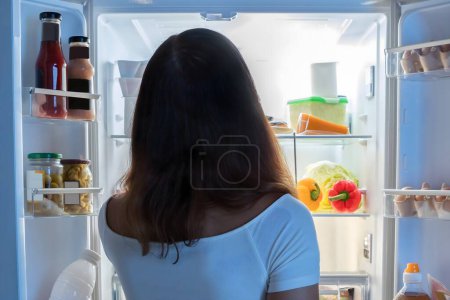 Foto de Vista trasera de mujer joven mirando en el refrigerador en la cocina - Imagen libre de derechos