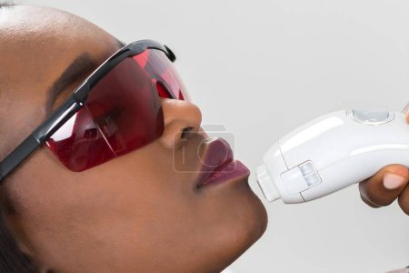 Téléchargez les photos : Gros plan de la jeune femme africaine recevant un traitement laser d'épilation sur le visage - en image libre de droit