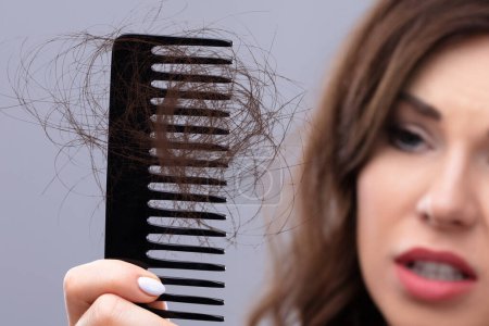 Primer plano de una mujer preocupada sosteniendo el peine que sufre de pérdida de cabello
