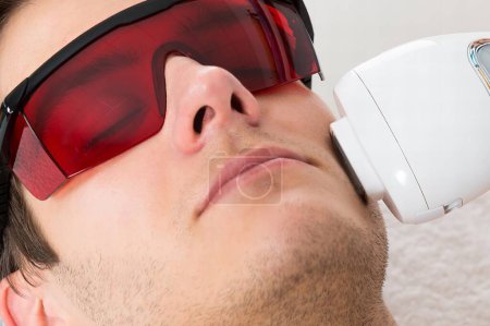 Téléchargez les photos : Jeune homme recevant un traitement d'épilation au laser au centre de beauté - en image libre de droit