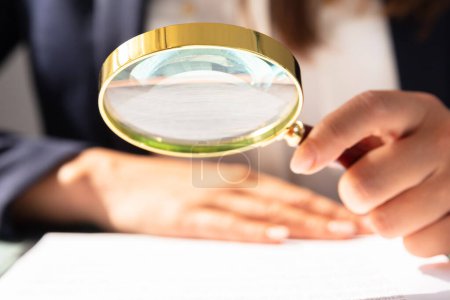 Téléchargez les photos : Gros plan de la main d'une femme d'affaires regardant le formulaire de contrat à travers le verre grossissant - en image libre de droit