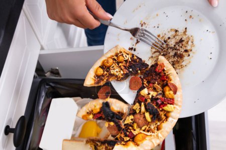 Téléchargez les photos : Gros plan d'une personne jetant une pizza Pepperoni sur une assiette dans la poubelle - en image libre de droit