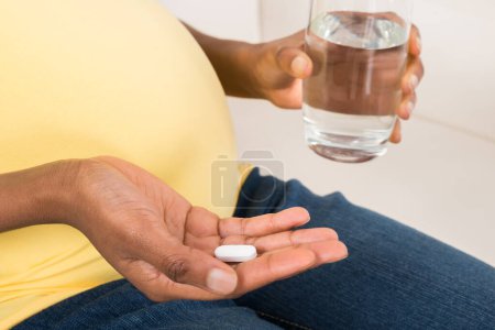 Foto de Primer plano de la mano de la mujer embarazada con vaso de agua y vitamina píldora - Imagen libre de derechos