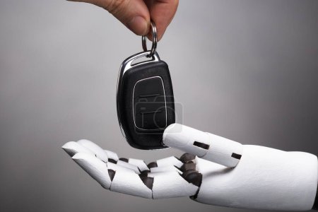 Photo for Close-up Of A Businessperson's Hand Giving Car Key To Robot On Grey Background - Royalty Free Image
