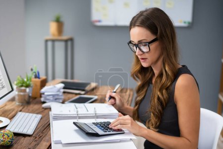 Photo for Close-up Of A Businessperson's Hand Calculating Invoice At Workplace - Royalty Free Image
