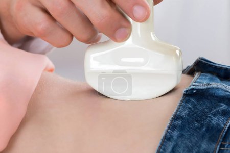 Foto de Primer plano del médico masculino que mueve la sonda de ultrasonido en el estómago de la mujer embarazada en el hospital - Imagen libre de derechos