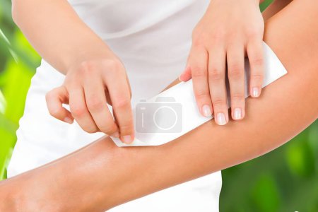 Foto de Sección media de la pierna de la mujer de cera esteticista con tira de cera en el spa de belleza - Imagen libre de derechos