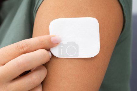 Téléchargez les photos : Femme appliquant patch sur son bras à la maison - en image libre de droit