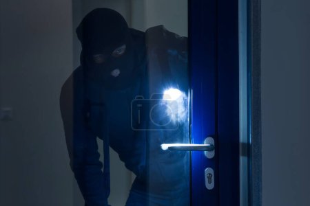 Foto de Ladrón con linterna tratando de romper la puerta de cristal con palanca - Imagen libre de derechos