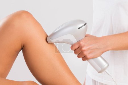 Téléchargez les photos : Section médiane de l'esthéticienne utilisant une machine laser sur la jambe du client au salon - en image libre de droit