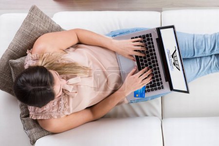 Téléchargez les photos : Jeune femme assise sur le canapé avec ordinateur portable Shopping en ligne - en image libre de droit