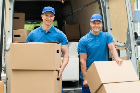 Foto de Dos felices trabajadores masculinos cargando pila de cajas de cartón en camión - Imagen libre de derechos