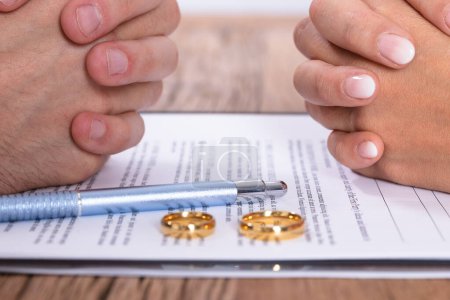 Mano de pareja con acuerdo de divorcio y anillos de boda dorados en escritorio de madera
