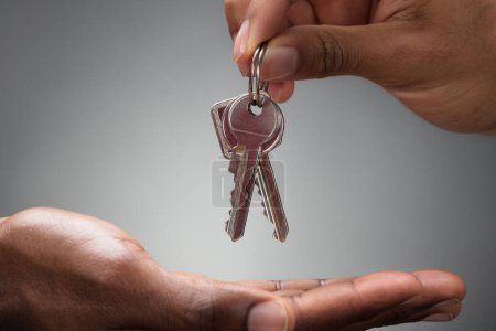 Photo for Close-up Of Hands Giving Keys Of An Apartment Against Gray Background - Royalty Free Image