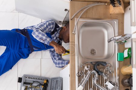 Vista de ángulo alto del Handyman que miente en el fregadero de reparación del piso en la cocina con la caja de herramientas
