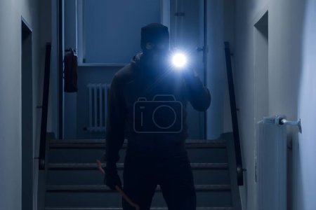 Photo for Full length of burglar with flashlight and crowbar in office corridor - Royalty Free Image
