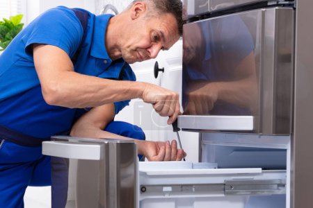 Téléchargez les photos : Homme mûr Serviceman Réparation réfrigérateur avec boîte à outils dans la cuisine - en image libre de droit