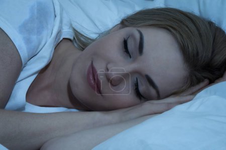 Foto de Mujer joven con manta durmiendo de noche en la cama - Imagen libre de derechos