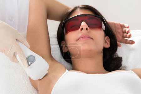 Téléchargez les photos : Femme recevant le traitement au laser d'épilation sur l'aisselle à la clinique de beauté - en image libre de droit