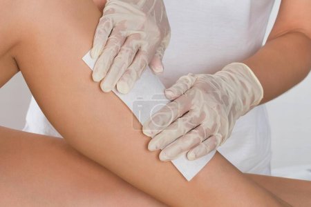 Téléchargez les photos : Esthéticienne épilation jambe de femme avec bande de cire à la clinique de beauté - en image libre de droit