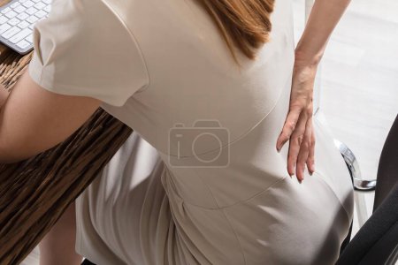 Photo for Young Businesswoman Having Back Pain Sitting On Chair At Workplace - Royalty Free Image