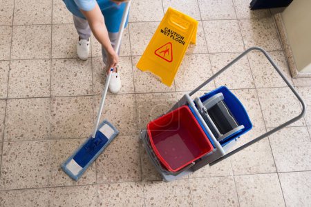 Téléchargez les photos : Femme étage de nettoyage de concierge avec des équipements de nettoyage et signe de plancher humide sur le plancher - en image libre de droit