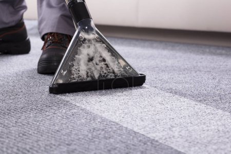 Foto de Sección baja de una persona limpiando la alfombra con aspiradora en la sala de estar - Imagen libre de derechos