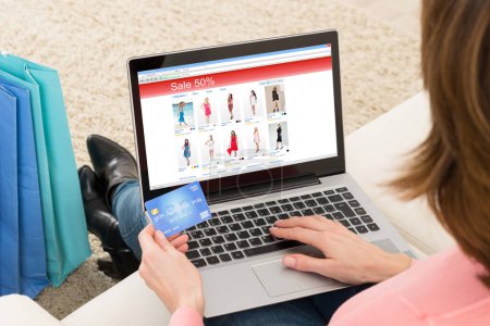 Téléchargez les photos : Jeune femme sur le canapé faisant du shopping en ligne avec carte de débit - en image libre de droit