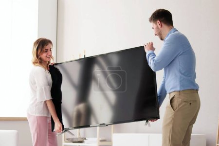 Téléchargez les photos : Heureux jeune couple portant avec enthousiasme leur nouvelle télévision - en image libre de droit