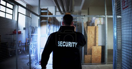 Foto de Guardia de seguridad caminando en el almacén sosteniendo linterna - Imagen libre de derechos