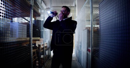 Foto de Guardia de seguridad caminando en el almacén sosteniendo linterna - Imagen libre de derechos