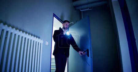 Téléchargez les photos : Gardien de sécurité mâle mature avec lampe de poche debout dans le couloir du bâtiment - en image libre de droit