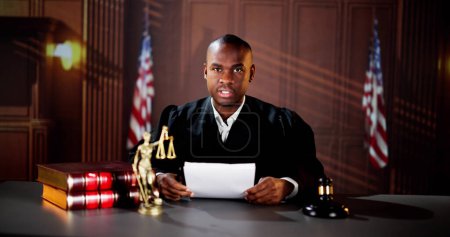 Téléchargez les photos : Juge masculin lisant des documents alors qu'il était assis au bureau dans la salle d'audience - en image libre de droit