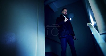 Téléchargez les photos : Gardien de sécurité mâle à la recherche sur escalier avec lampe de poche - en image libre de droit